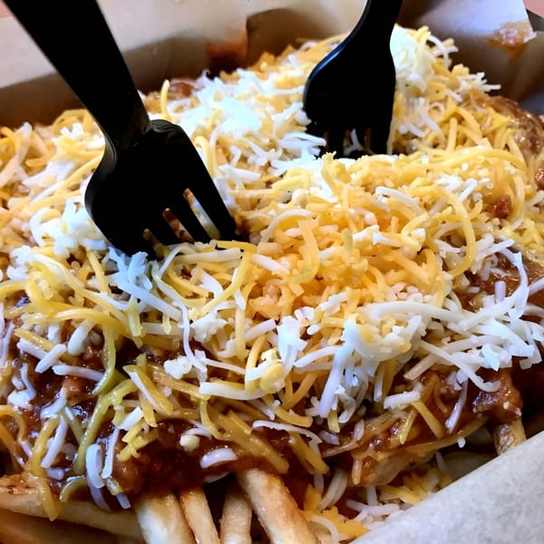 Everest Burgers' chili cheese fries, topped with shredded cheddar and Monterey Jack, with two black forks.
