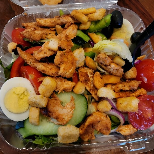 A close-up of a Everest Burgers chicken salad with croutons, tomatoes, cucumbers, and hard-boiled egg.