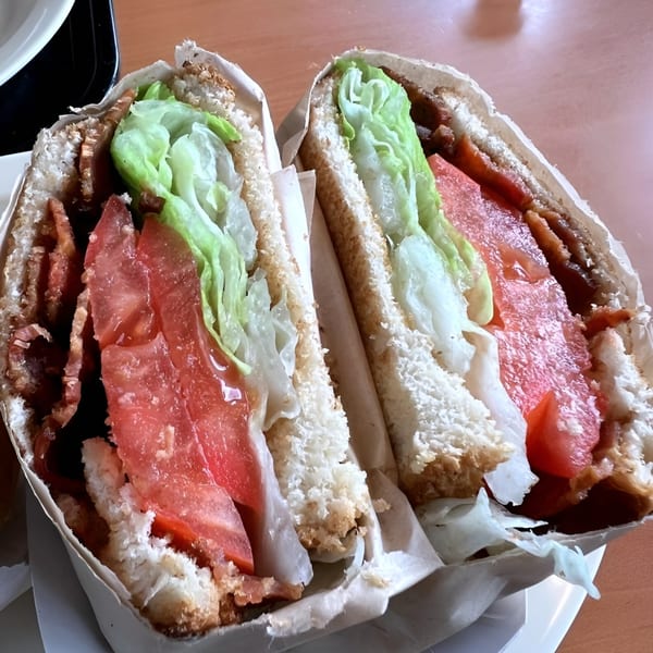 A bacon, lettuce, and tomato sandwich, cut in half, wrapped in paper.